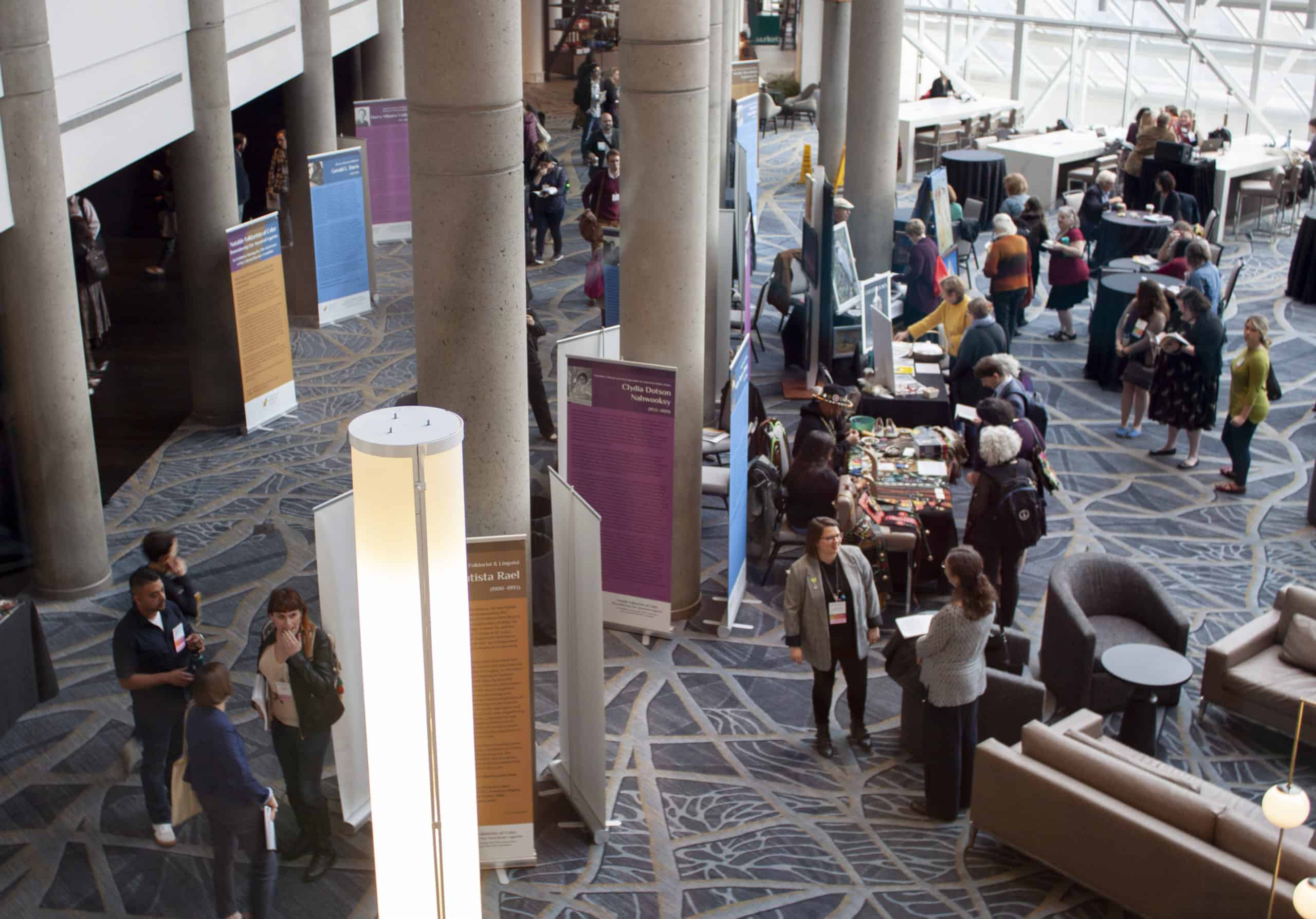 View from above of many people gathered in a hotel lobby around posters and exhibit tables