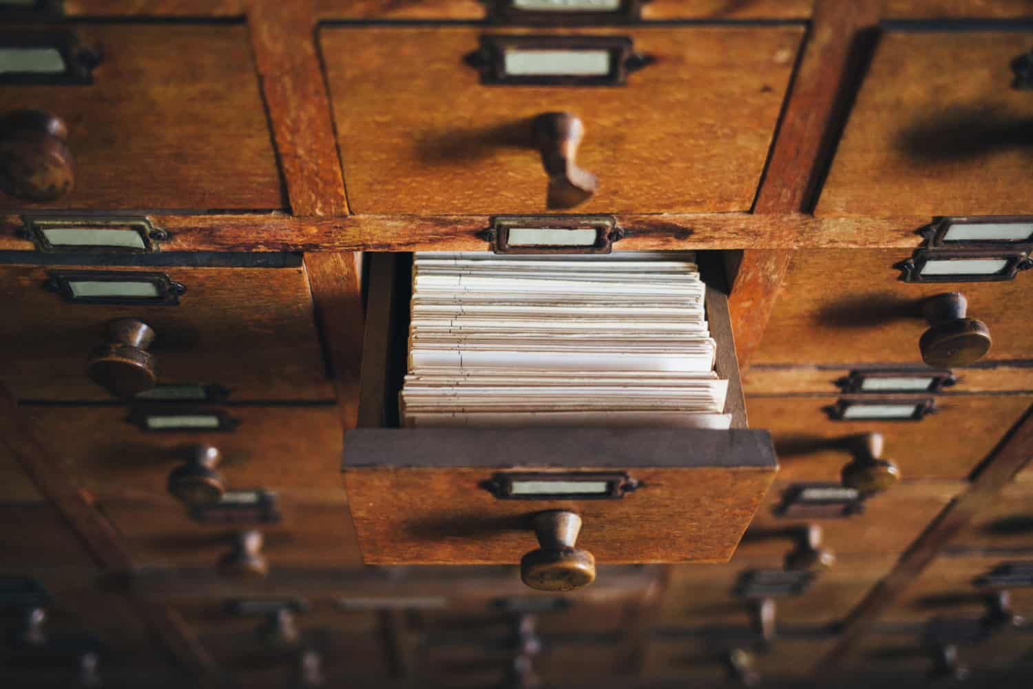 An open drawer in a wooden card catalog case shows the tops of cards