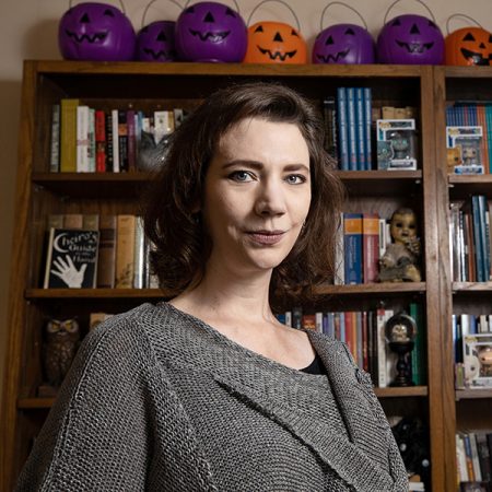kitta sitting in front of a bookshelf with jack-o-lanterns in the background