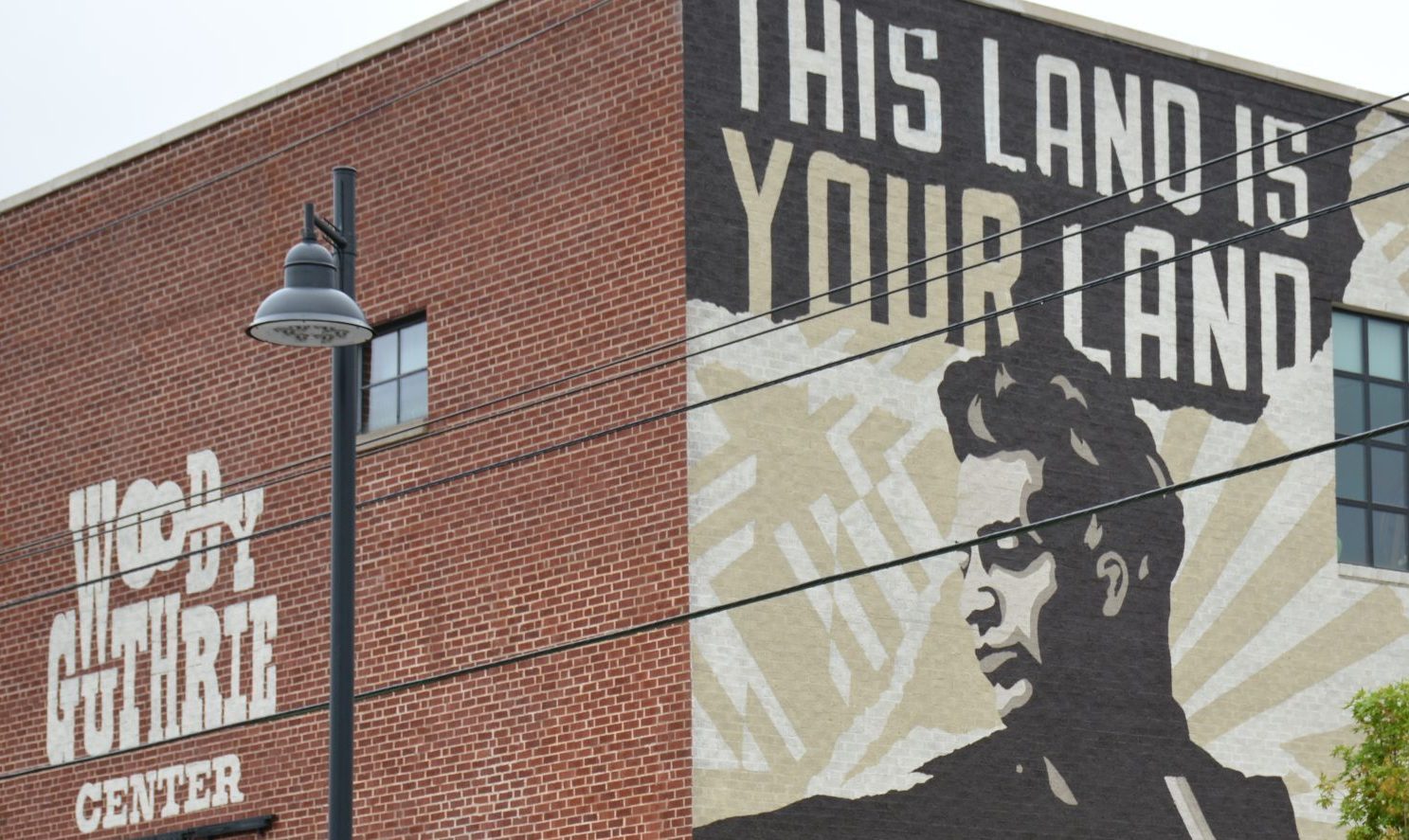 A mural of folk musician Woody Guthrie featuring an image of Guthrie playing guitar, below the text "The Land is Your Land".