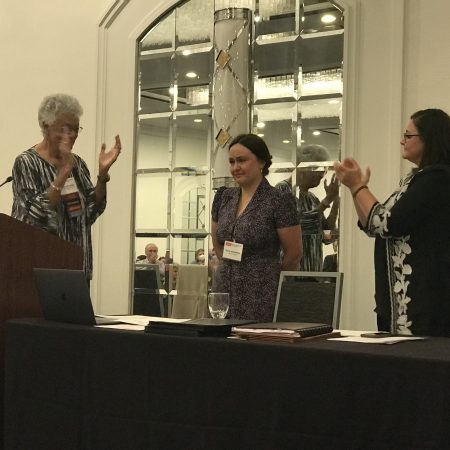 Photo of Marilyn White presenting Iryna Voloshyna with the inaugural Presidential Award for Meritorious Service. Jessica Turner and Marilyn White are clapping.