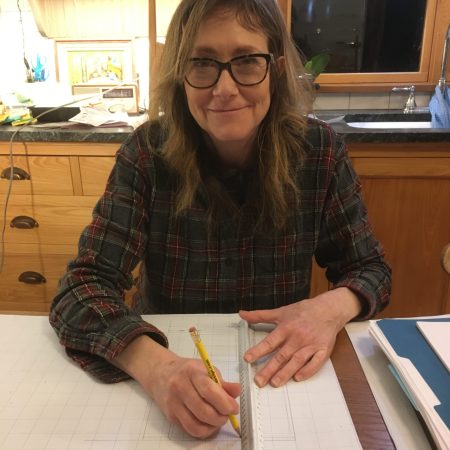Nancy Hiller sitting at a table with pencil and ruler in her hands with a sheet of paper underneath them on the table