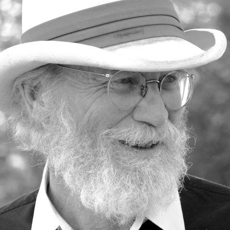a white-bearded person wearing glasses and a hat with a trim