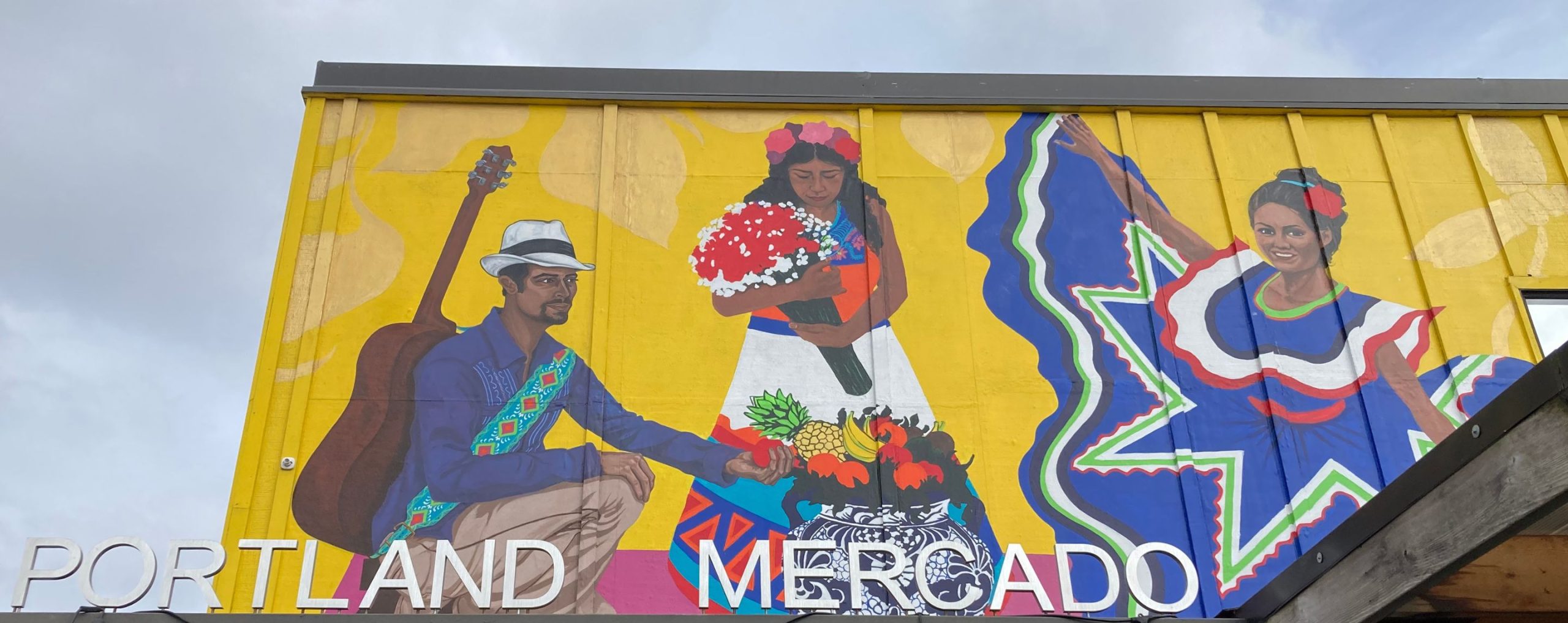 portland mercado front entrance, which has a yellow background and three people playing music and dancing